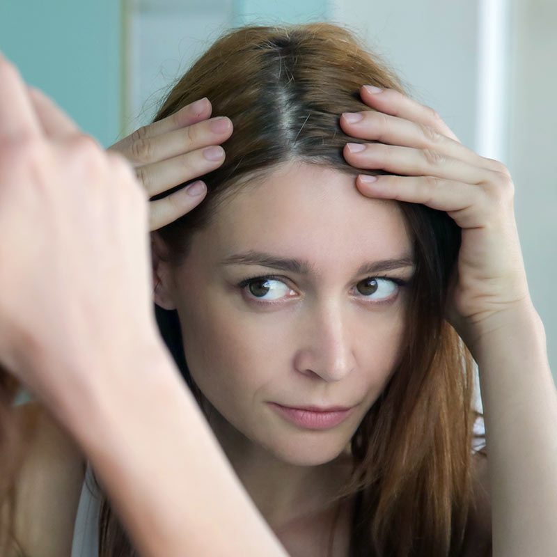 Young woman checking her dry scalp in the mirror